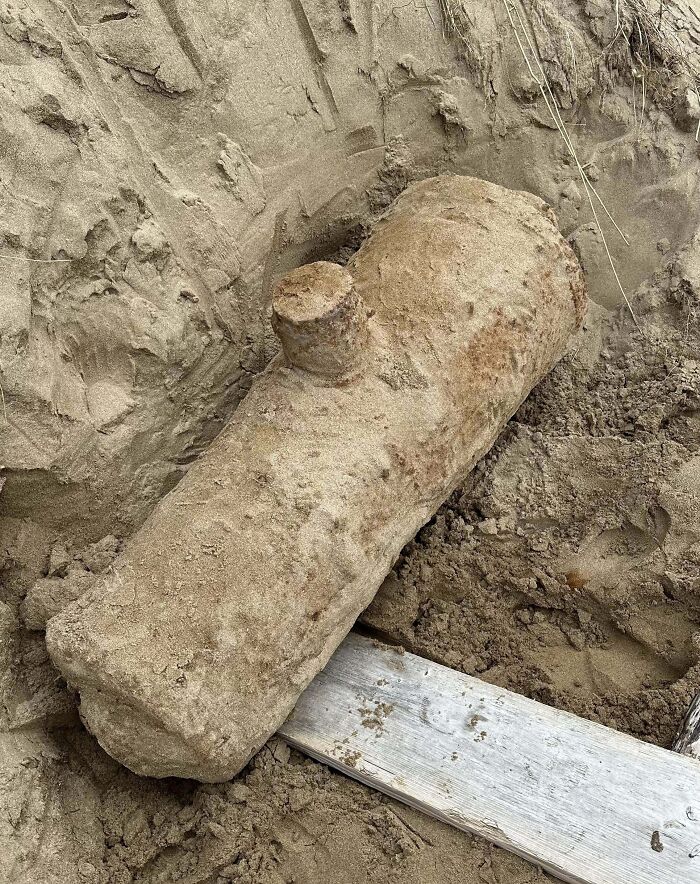 Large mysterious object covered in dirt partially unearthed from sandy soil, intriguing people who stumbled upon it.