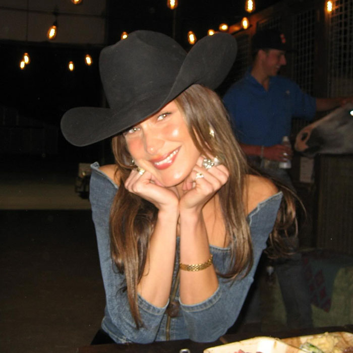 Woman wearing a black cowboy hat smiling at a table, related to famous people accused of having plastic surgery.