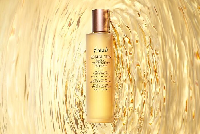 Beauty brand Fresh Kombucha facial treatment essence bottle with golden liquid background highlighting skincare in 2024.