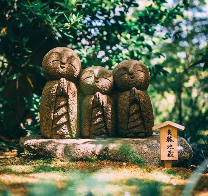 Three smiling stone statues in a serene garden, showcasing unique cultural art from Japan in a peaceful outdoor setting.