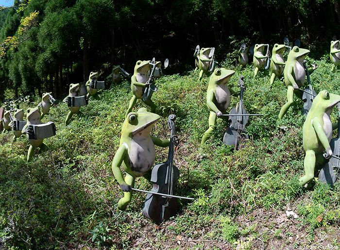 Frog statues playing musical instruments in a lush garden, exemplifying quirky and interesting Japan culture.