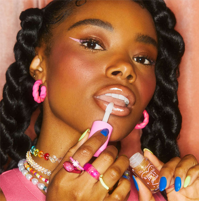 Close-up of a woman applying lip gloss, showcasing beauty brands setting the gold standard in 2024 trends.