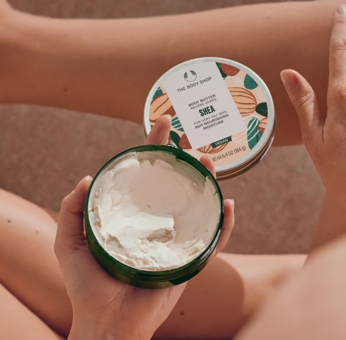 Open container of shea body butter from a top beauty brand held by a person applying skincare in natural light.