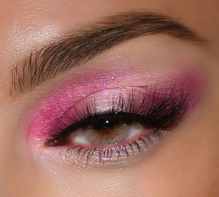 Close-up of an eye with glittery pink eyeshadow and long lashes showcasing beauty brands setting the gold standard in 2024.