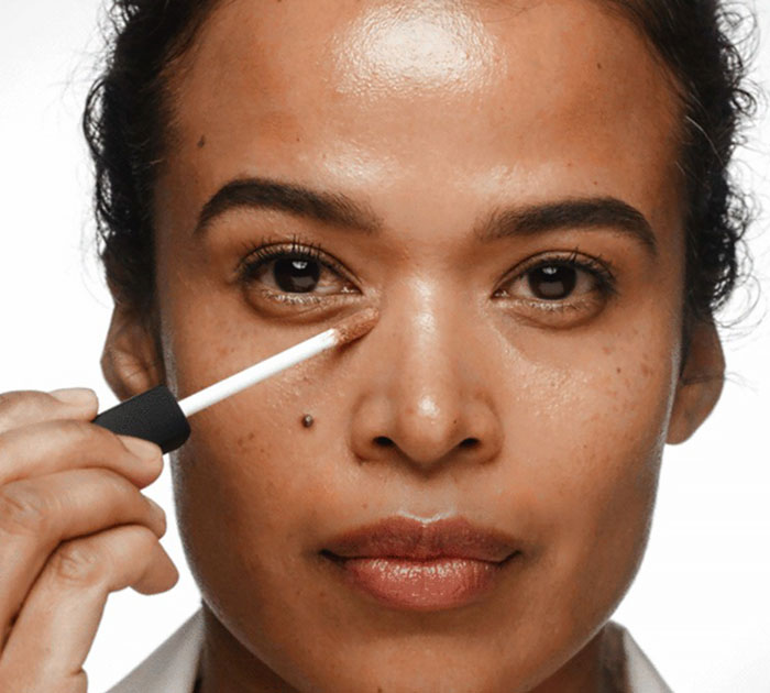 Close-up of woman applying makeup under eye, representing top beauty brands setting the gold standard in 2024.