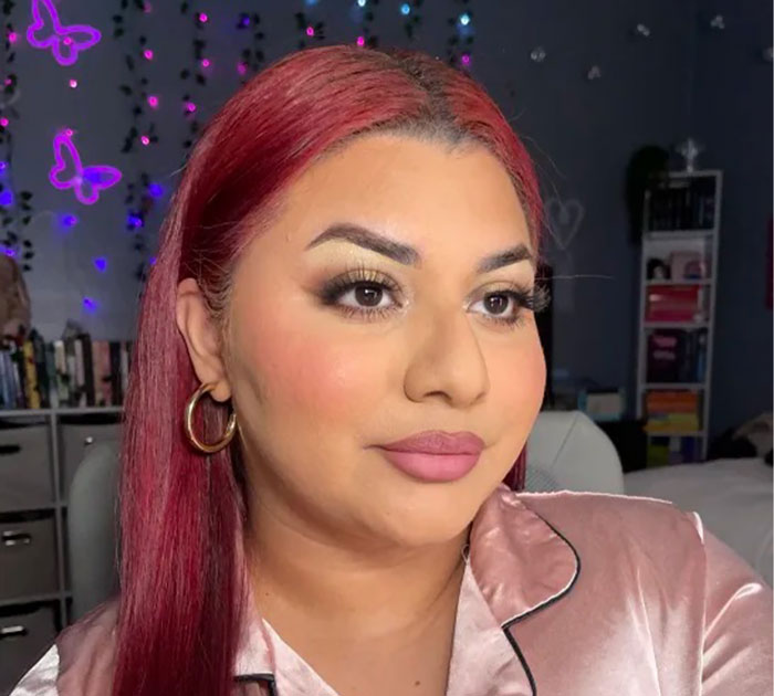 Woman with red hair and flawless makeup showcasing beauty brands setting the gold standard in 2024 in a cozy room.