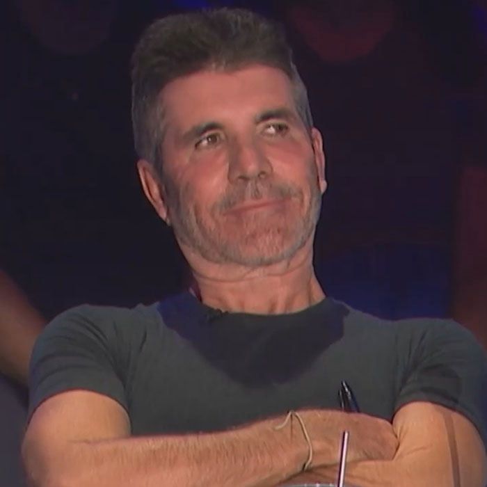 Man with folded arms sitting and appearing thoughtful in a dark setting related to famous people accused of plastic surgery.