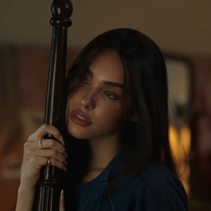 Young woman with dark hair holding a wooden post, illustrating famous people accused of having plastic surgery.