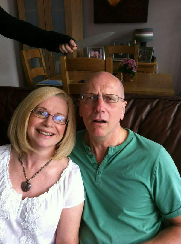 a couple taking a photo with a hand holding a knife behind their backs 