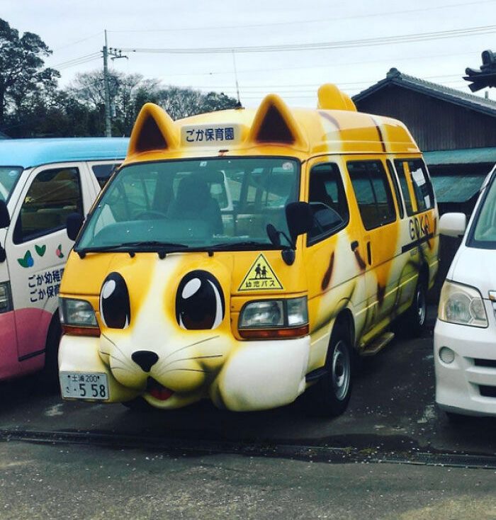 Yellow van designed as a cartoon cat with large eyes and ears parked among other vehicles in Japan.