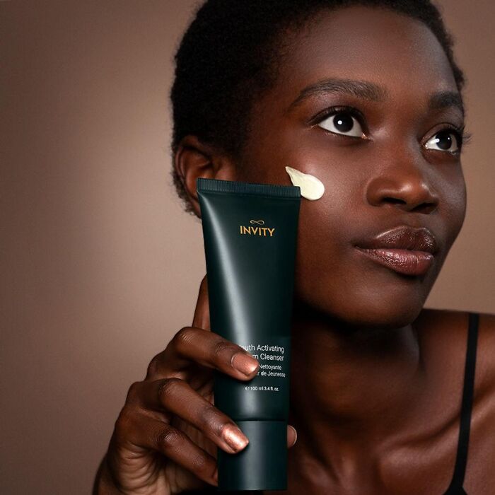 Dark-skinned woman applying moisturizer with skincare product from beauty brands setting the gold standard in 2024.
