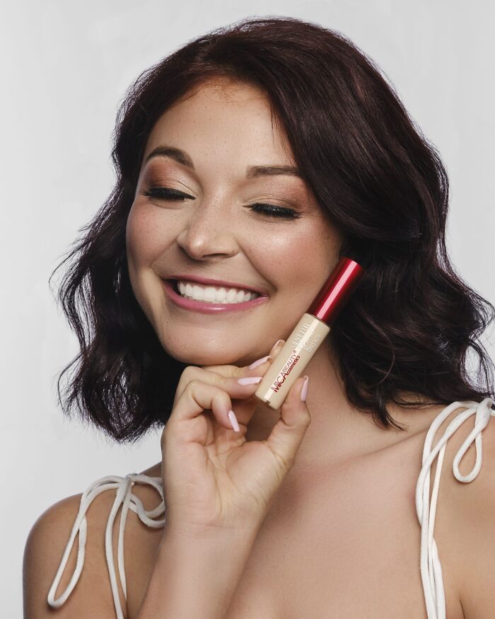 Smiling woman holding concealer makeup product, showcasing beauty brands setting the gold standard in 2024.
