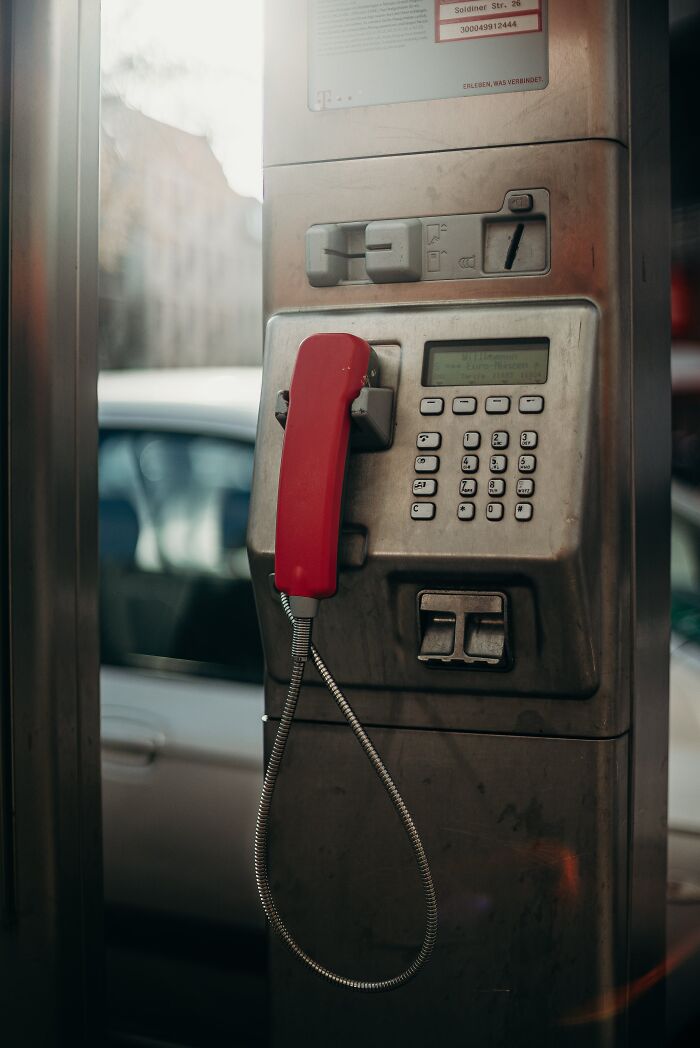 Old public payphone with a red handset in an outdoor booth, illustrating trivia-worthy facts about the past.