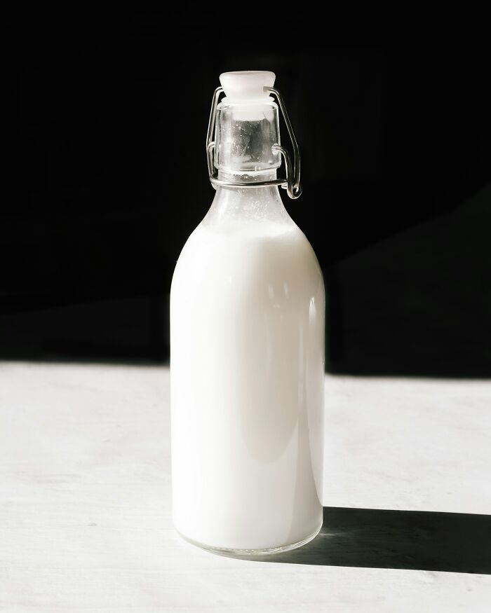 Glass bottle filled with milk casting a shadow on a white surface, illustrating trivia-worthy facts about the past.