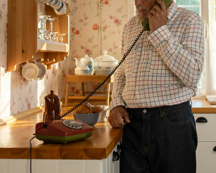 Older man using a vintage rotary phone in a retro kitchen, illustrating trivia-worthy facts about the past.