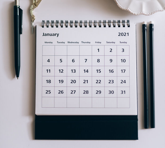 Spiral desk calendar open to January 2021 surrounded by pens and pencils, illustrating advice timing concept.