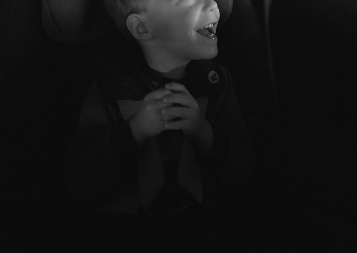 Young child laughing and clasping hands in a dark setting, illustrating curiosity about trivia-worthy facts from the past.