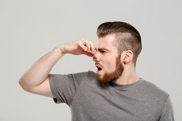 Man in a gray shirt holding his nose, reacting to a bad odor, highlighting cat poop smell issues.