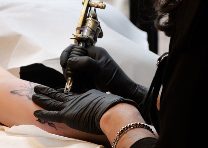 Tattoo artist in gloves creating a floral design on a client's arm.