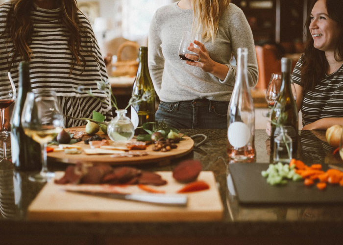 Three women over 40 enjoying wine and snacks, discussing their childfree life choices in a cozy kitchen setting.