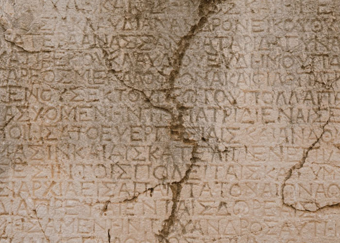 Ancient stone tablet engraved with Greek text showing detailed weathered inscriptions and cracks on surface.