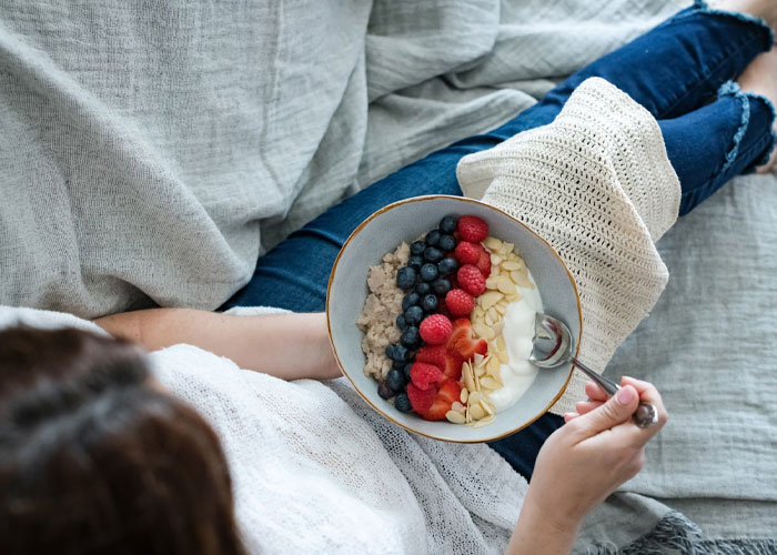 Person relaxing on couch holding a bowl of yogurt with berries and nuts, illustrating people confess things late in life.