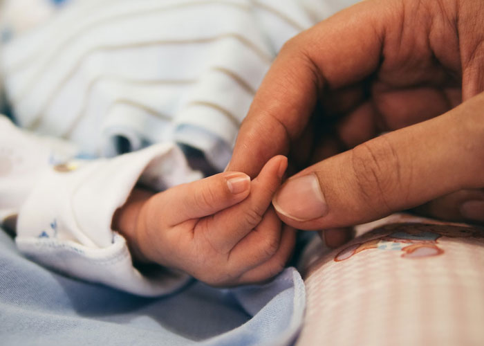Close-up of an adult hand gently holding a baby’s hand, highlighting a contrast for childfree people over 40 life choices.