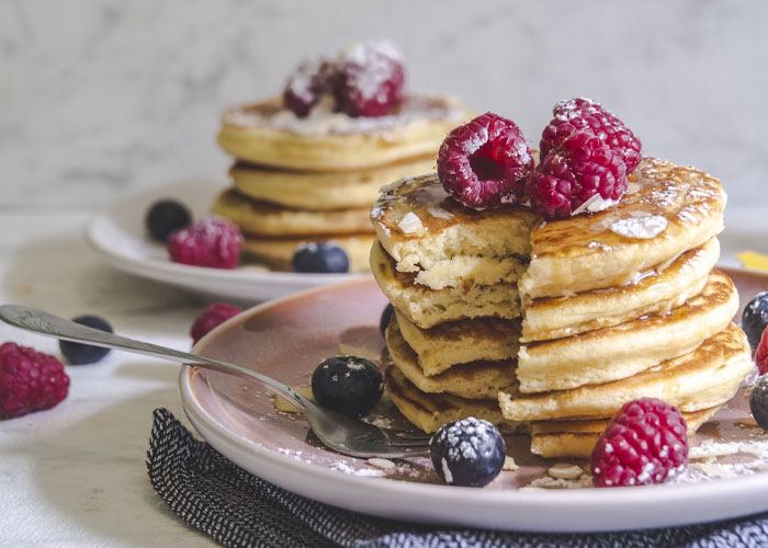 Stack of fluffy pancakes topped with raspberries and powdered sugar, illustrating things people didn’t know late in life.