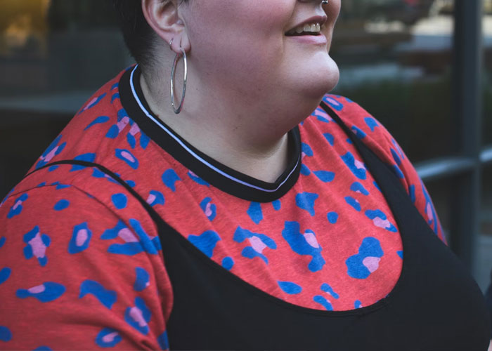 Woman wearing a colorful shirt and hoop earrings, smiling outside a building.