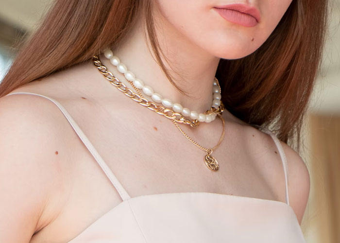 Young woman wearing layered gold and pearl necklaces, highlighting stylish jewelry trends and personal accessories.