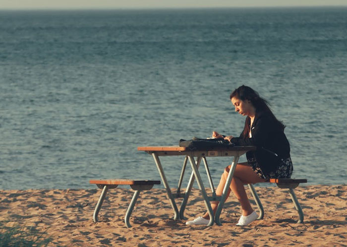 Woman over 40 writing at a picnic table on the beach, reflecting on life choices as a childfree person.