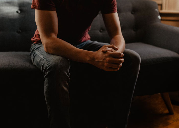 Person sitting on a dark couch with clasped hands, illustrating people confessing things they didn't know late in life.
