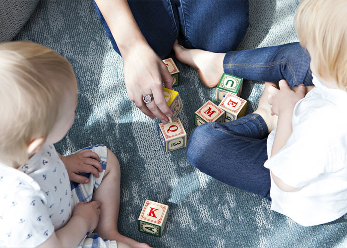 Adult with children playing with alphabet blocks on a carpet, illustrating themes of childfree people over 40 and life choices.