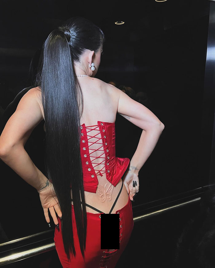 Katy Perry in red lace-up outfit showing tattoo and thong.