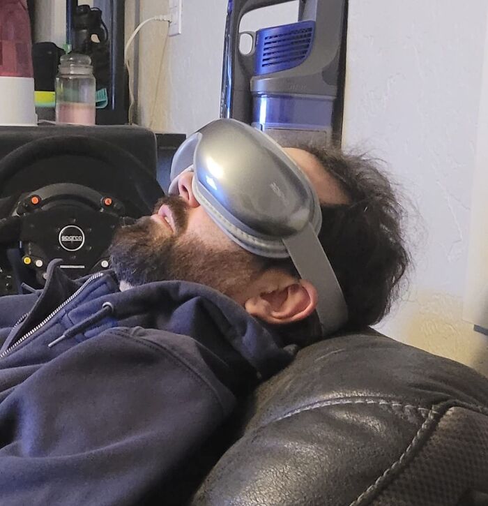 Man wearing a gray sleep mask resting on a couch with headphones and speaker in a casual room setting.