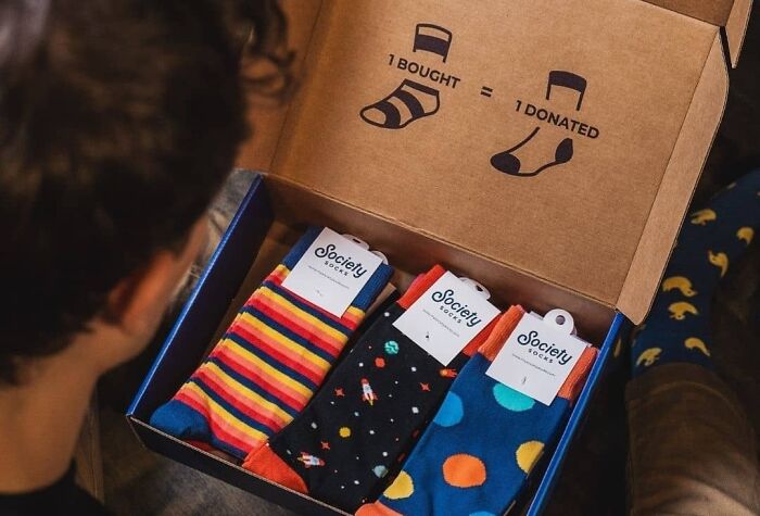Colorful subscription socks gift box, promoting buy-one-donate-one charity model, viewed by a person.