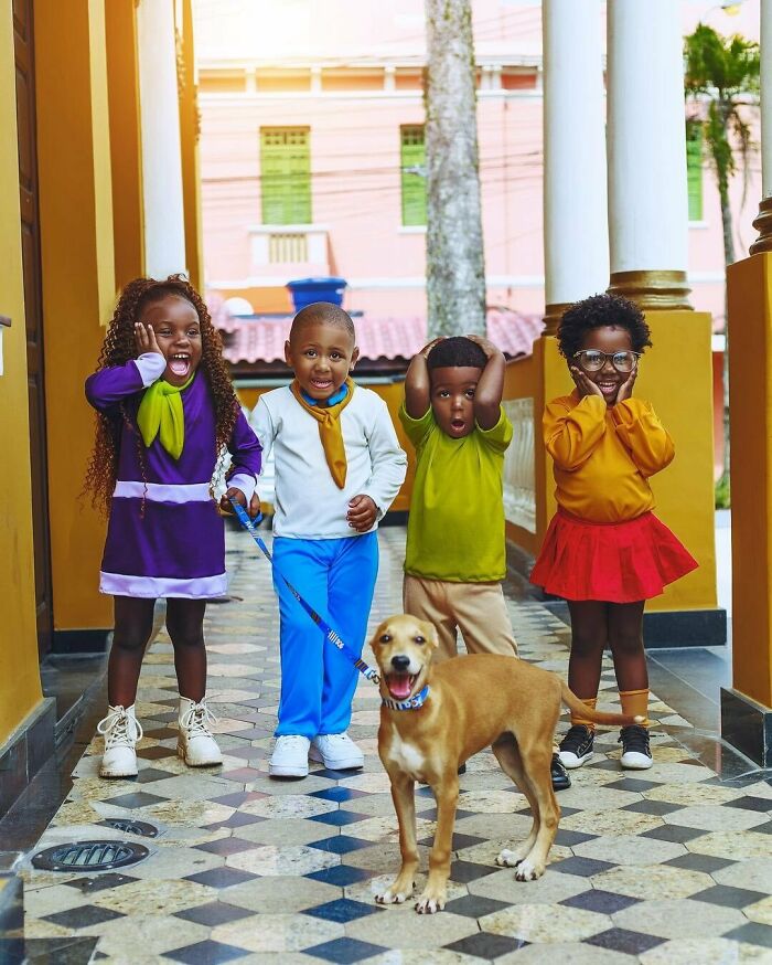 Niños sorprendidos jugando con un perro feliz en un pasillo colorido con baldosas decorativas y columnas blancas.