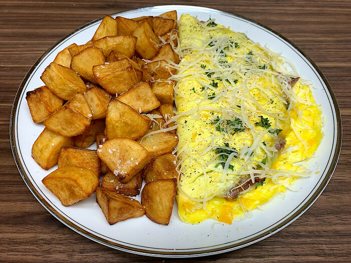 Perfectly cooked omelette topped with cheese and herbs served with golden crispy fried potatoes on a white plate.