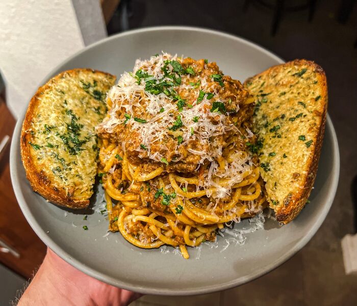 Plate of spaghetti with meat sauce topped with grated cheese and parsley, served with two slices of garlic bread, food perfection.