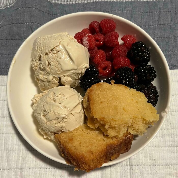 Bowl with two scoops of ice cream, fresh raspberries and blackberries, and two pieces of moist cake showing food perfection.