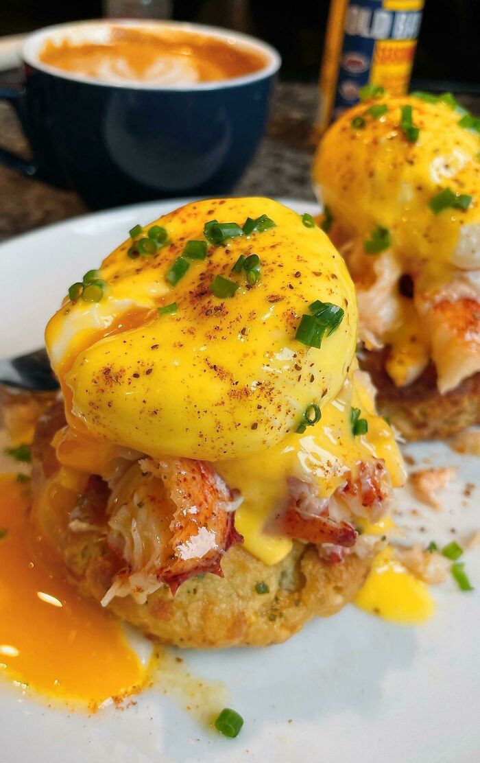 Eggs Benedict with hollandaise sauce and chives served on a biscuit, showcasing food perfection and a coffee in the background.