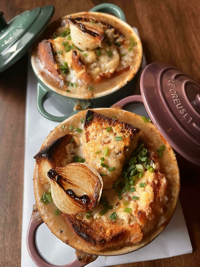Two bowls of perfectly baked French onion soup with melted cheese, toasted bread, and garnished with chives and onions.