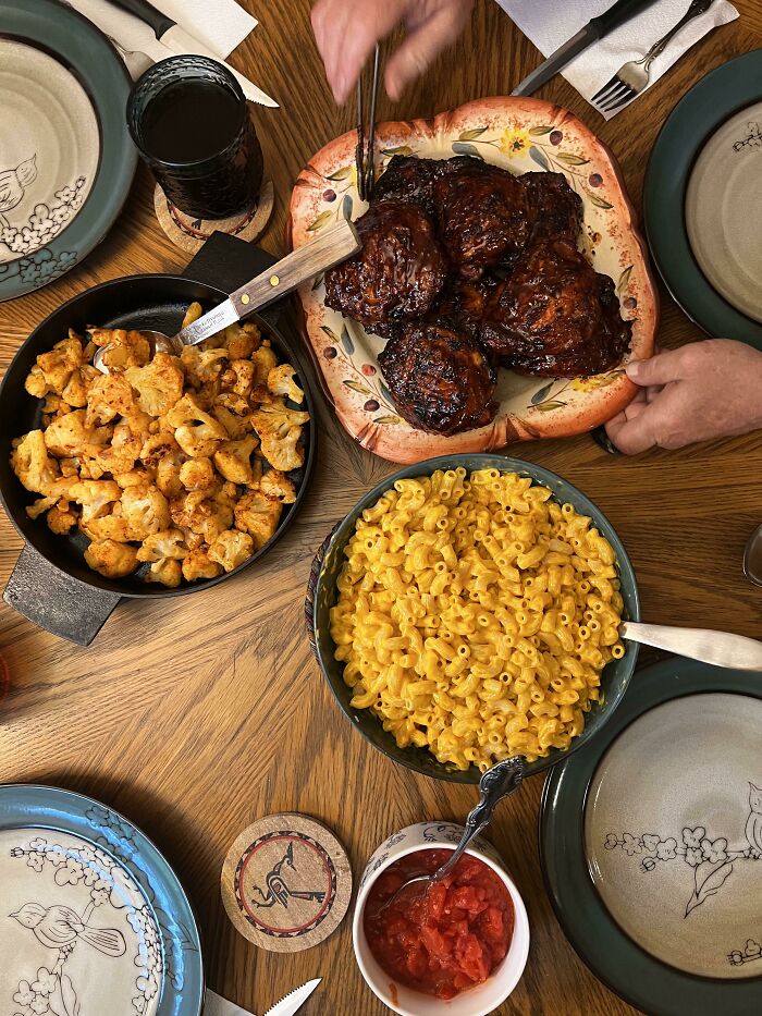 Perfectly cooked barbecue chicken with roasted cauliflower and creamy mac and cheese served on a wooden table.