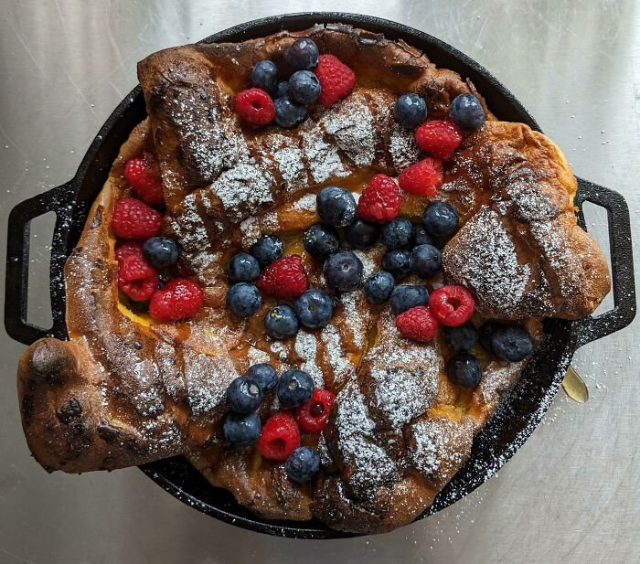 Perfectly baked dessert in a cast iron skillet topped with fresh blueberries, raspberries, and powdered sugar achieving food perfection.