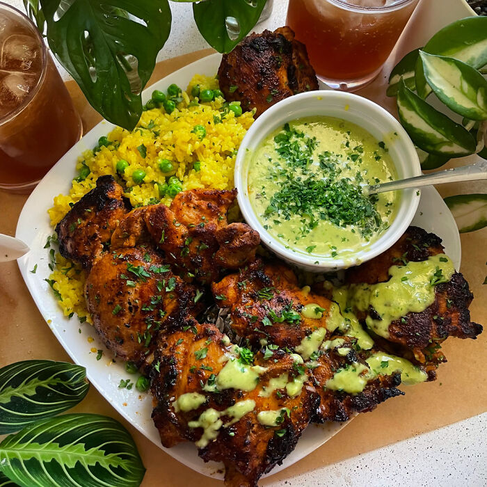 Grilled chicken with green sauce, yellow rice with peas, and iced tea, showcasing perfection in food presentation.