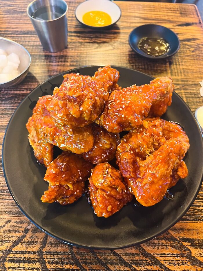 Crispy fried chicken wings perfectly coated with sauce and sprinkled with sesame seeds on a black plate for food perfection.