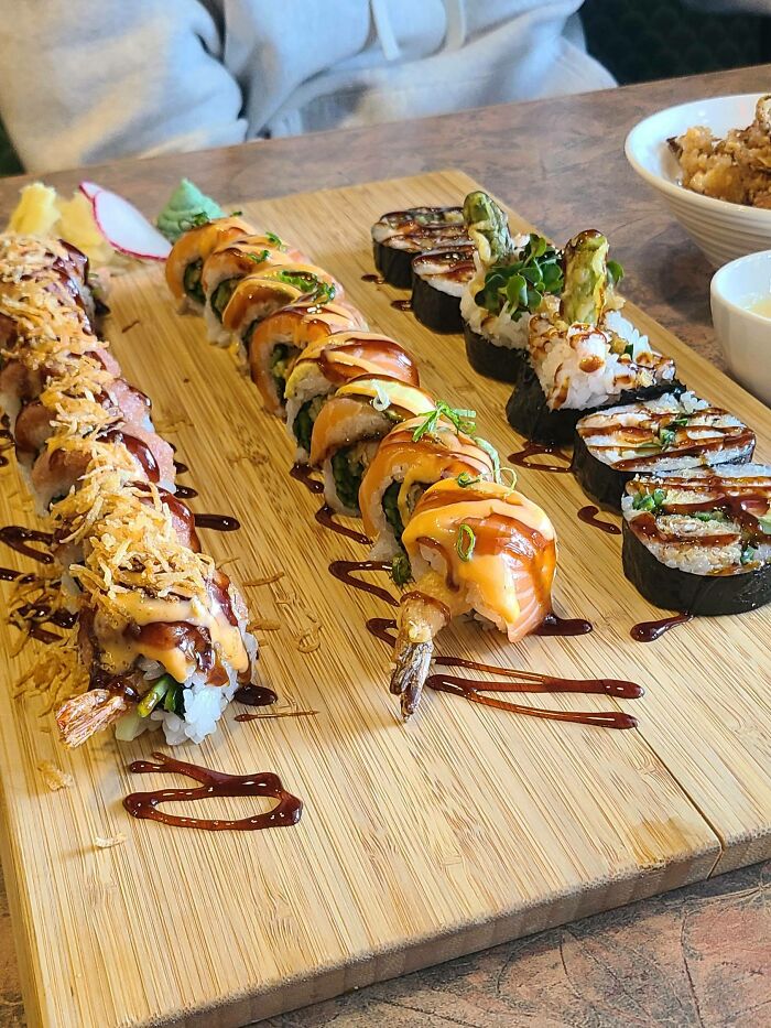 Perfectly arranged sushi rolls with sauces and garnishes on a wooden board showcasing food perfection.