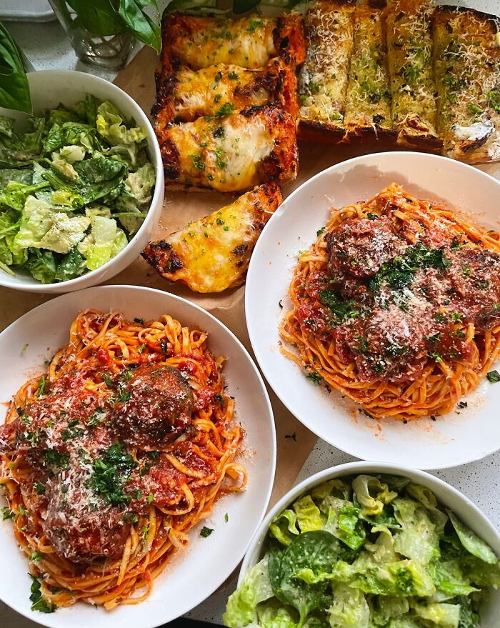 Two plates of perfectly cooked spaghetti and meatballs with garlic bread and fresh green salads displayed on a table