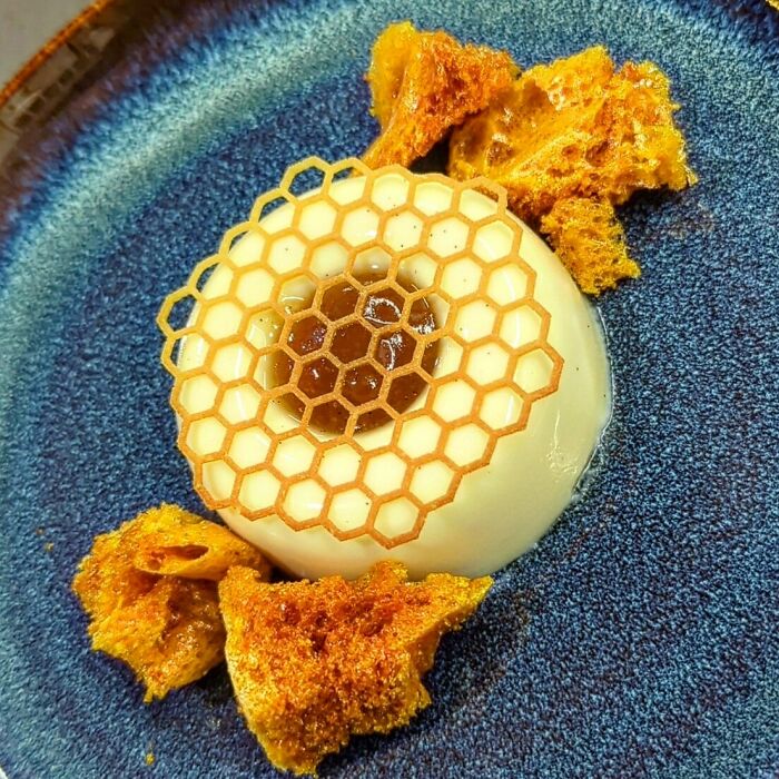 A perfectly plated dessert with honeycomb-patterned garnish and crunchy honeycomb pieces on a blue ceramic plate.