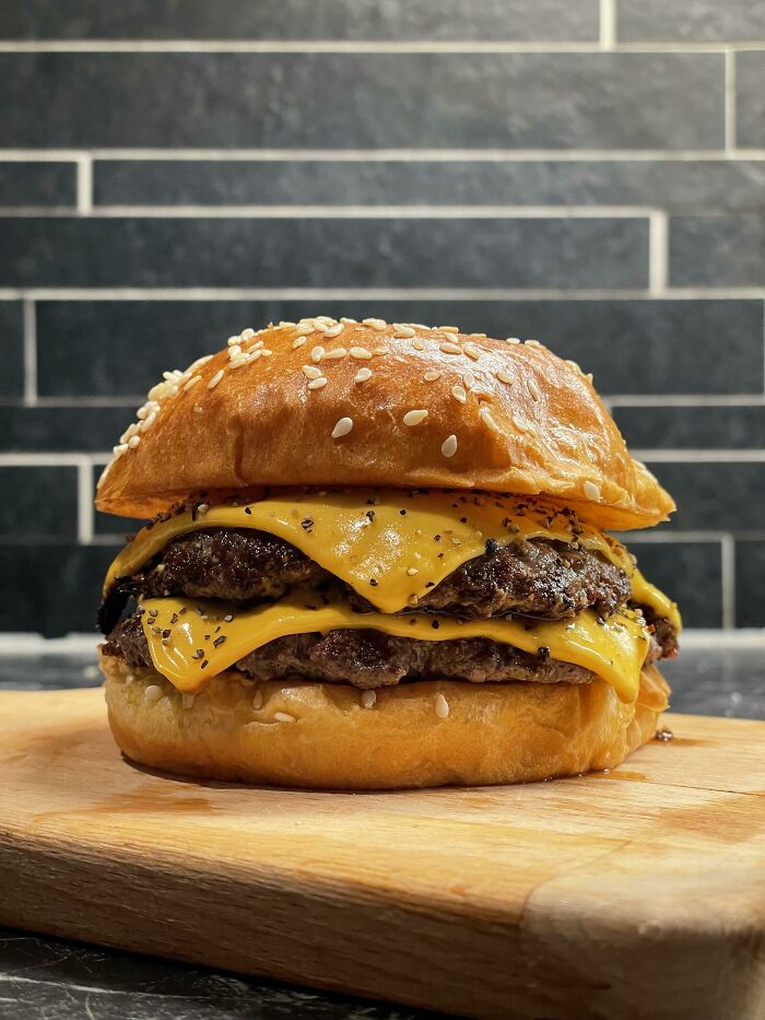 Perfectly made cheeseburger with double beef patties and melted cheese on a sesame seed bun, showcasing food perfection.